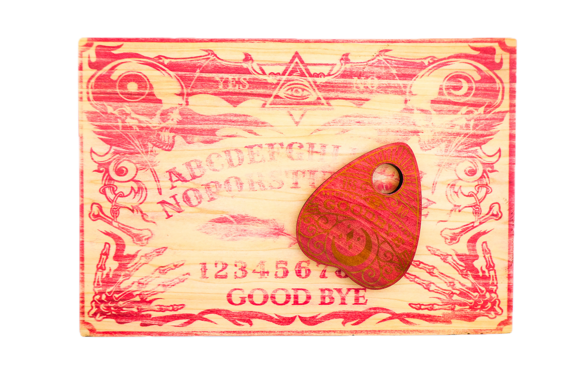 A carved wooden Ouija board with red-painted details and a matching wooden planchette resting on top.