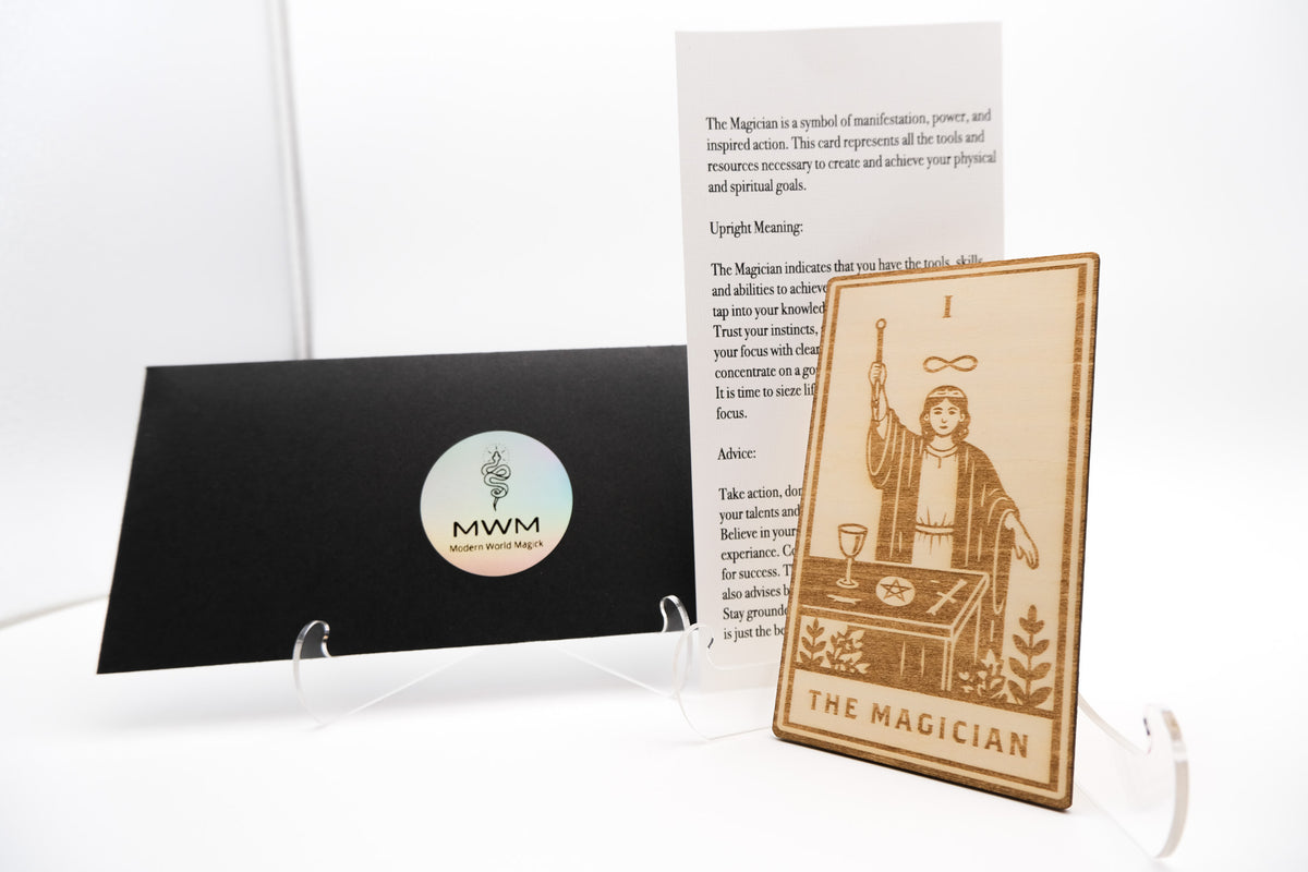 A tarot card set featuring 'The Magician' card displayed on a clear acrylic stand, next to a black card holder with a circular 'MWM Tarot Cards' logo, and an instruction card on a white background.