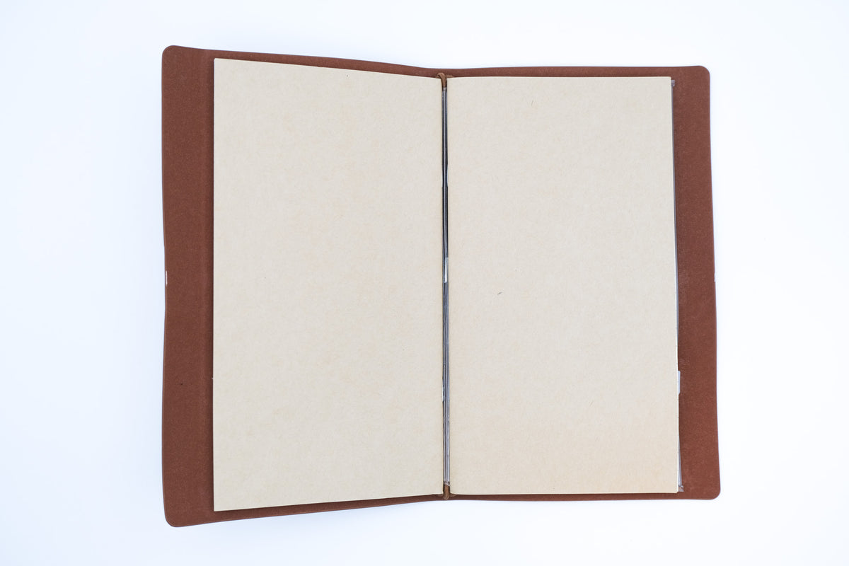 An open notebook or journal with blank beige pages and a brown cover, photographed from above on a clean white background.