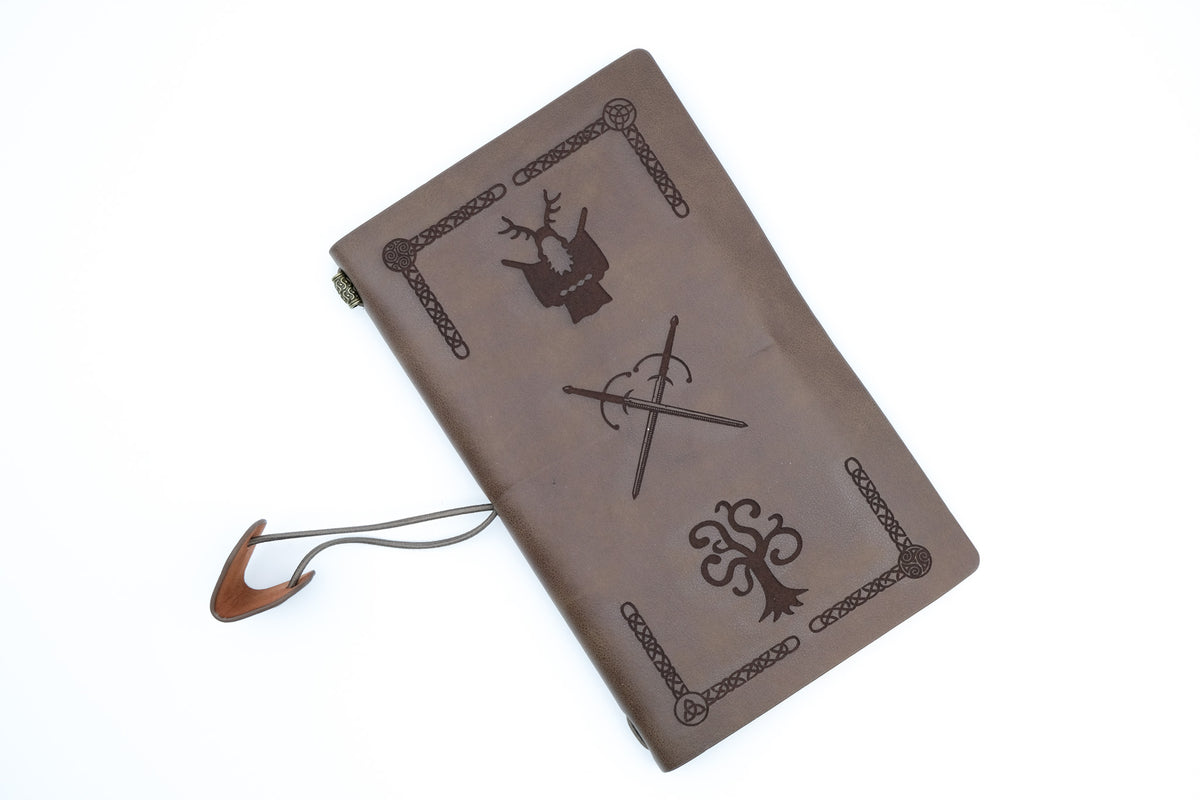 A brown leather-bound journal with embossed heraldic symbols, including a deer, sword, and tree, on a plain white background.
