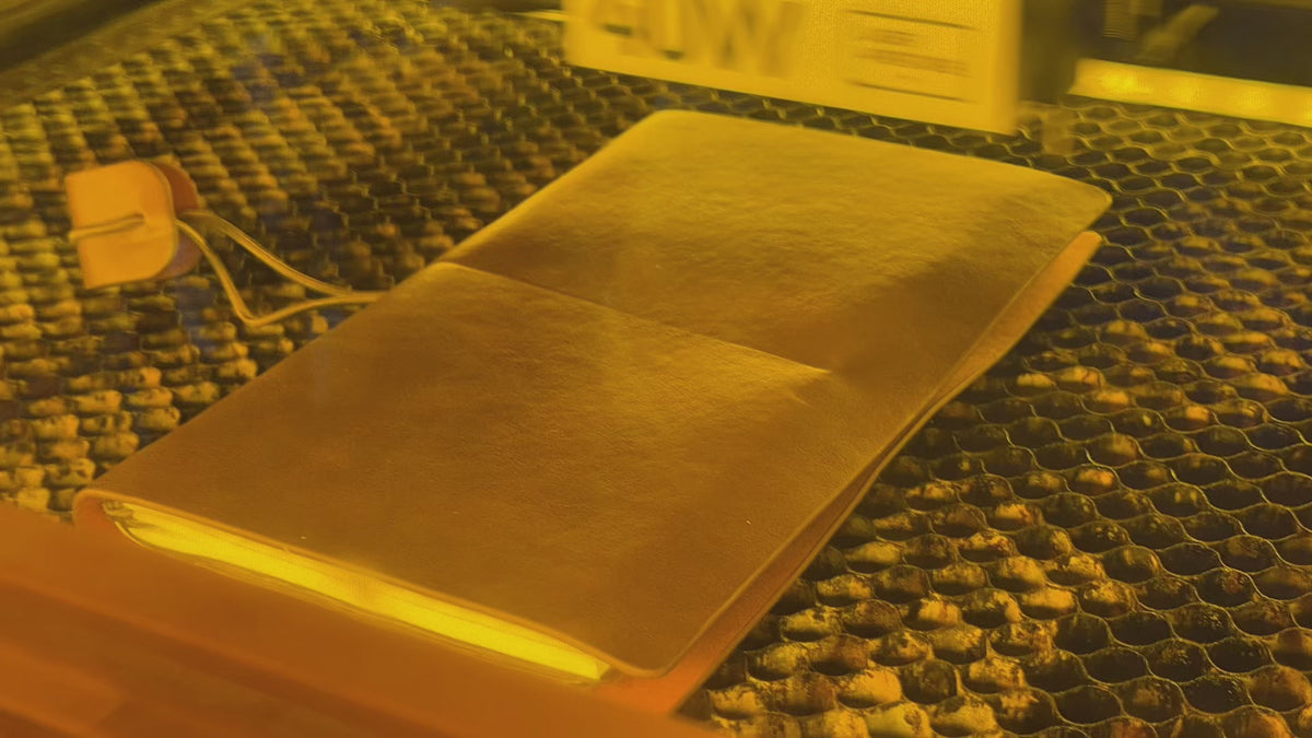 Laser engraver in process of engraving druidry symbols on a brown leather notebook.