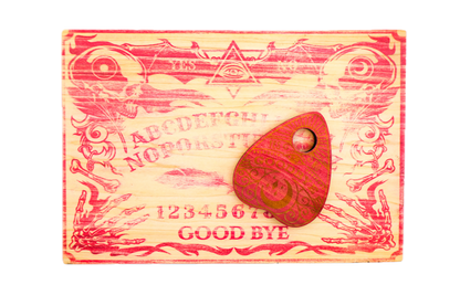 A carved wooden Ouija board with red-painted details and a matching wooden planchette resting on top.