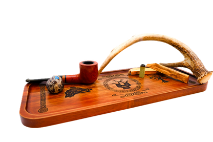 A rectangular wooden serving tray with a warm reddish-brown finish, featuring dark engraved symbols: a boar's head on the left, Cernunnos medallion, tree of life on the right, flanked by knotted pillar borders holding a reddish-brown smoking pipe, a small marbled glass bowl, and a curved antler.